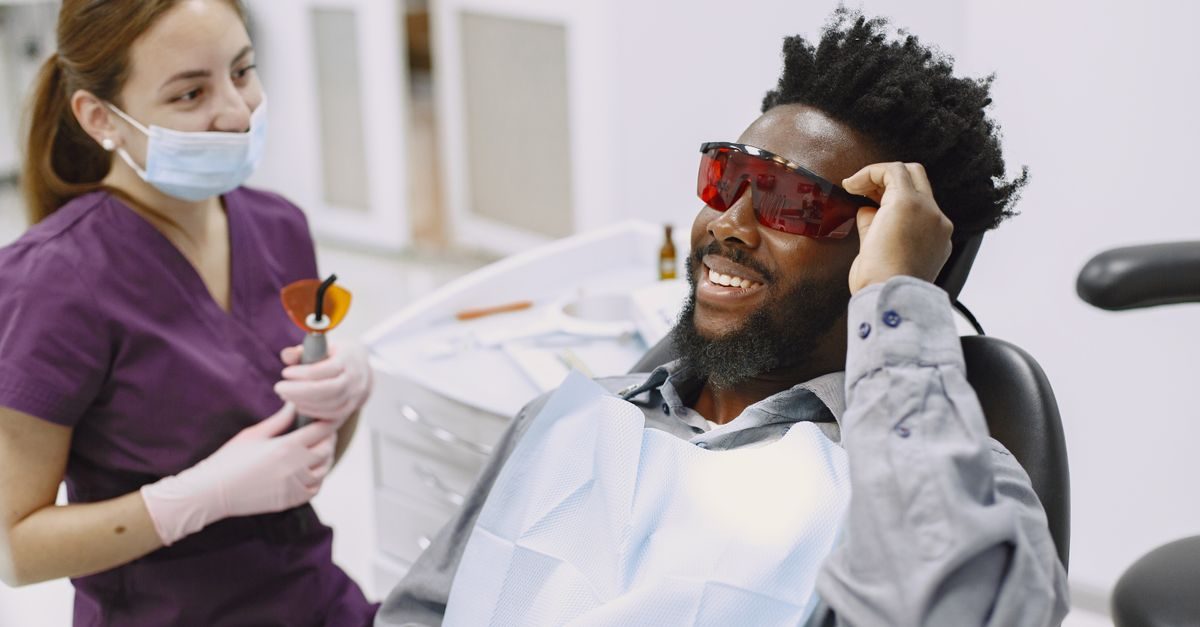 Eine Zahnärztin mit Mundschutz und ein lächelnder Patient mit roter Schutzbrille in einer hellen Zahnarztpraxis