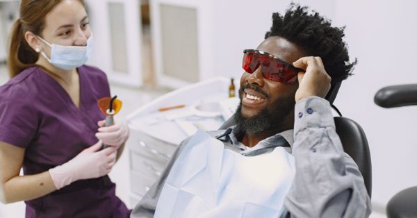 Eine Zahnärztin mit Mundschutz und ein lächelnder Patient mit roter Schutzbrille in einer hellen Zahnarztpraxis