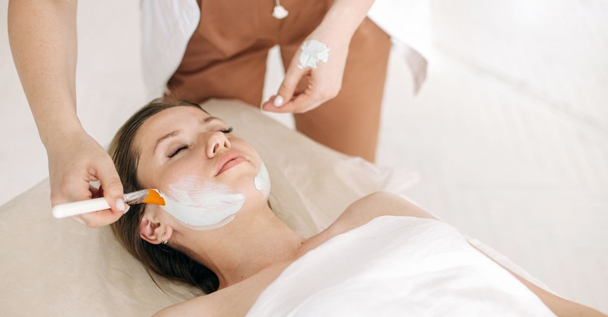 Una esteticista aplica una mascarilla facial con brocha a una clienta relajada en un centro de belleza