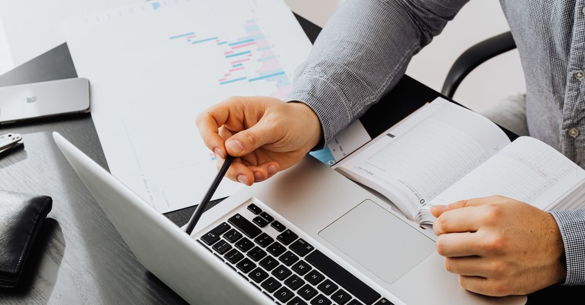 Eine Person arbeitet konzentriert an einem Schreibtisch mit Laptop, Notizbuch und statistischen Unterlagen