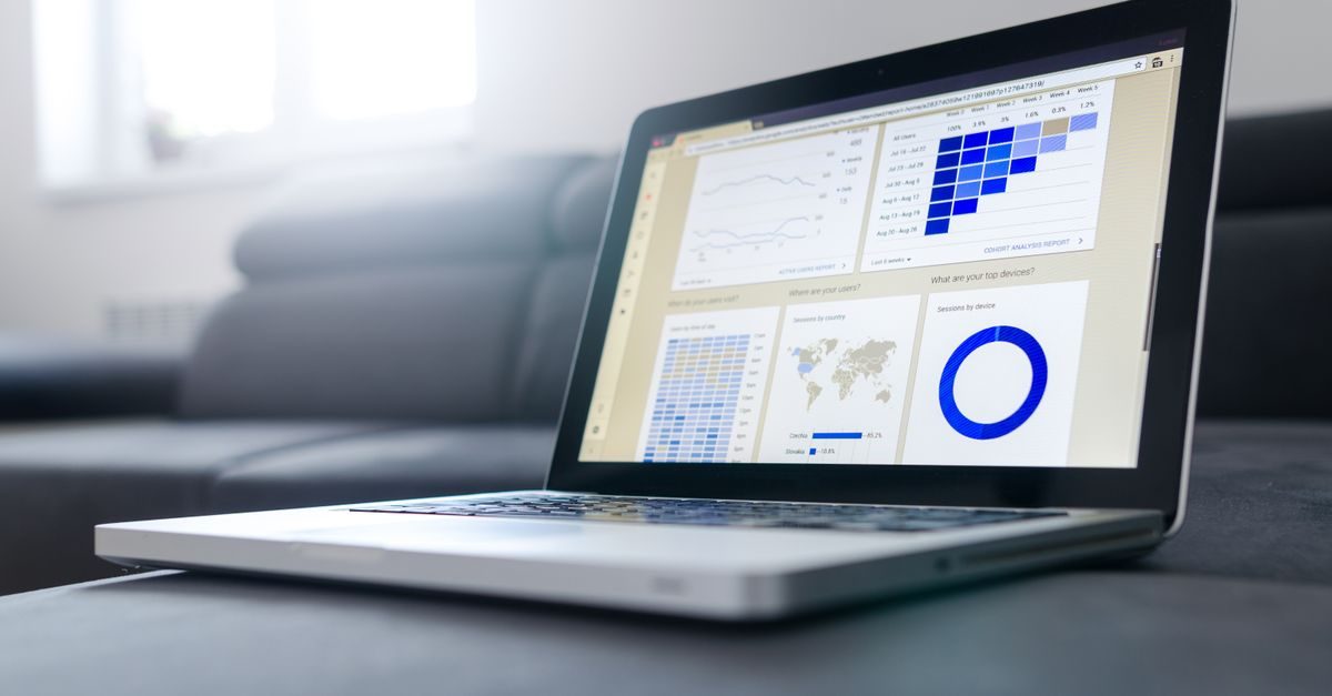 A laptop screen displaying business analytics dashboards with charts and graphs sits on a dark surface in a bright room