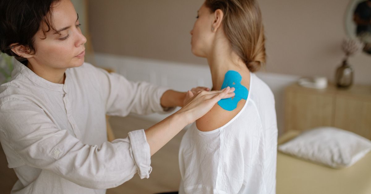 A physiotherapist applies blue kinesiology tape to a patient's shoulder in a calm clinic setting