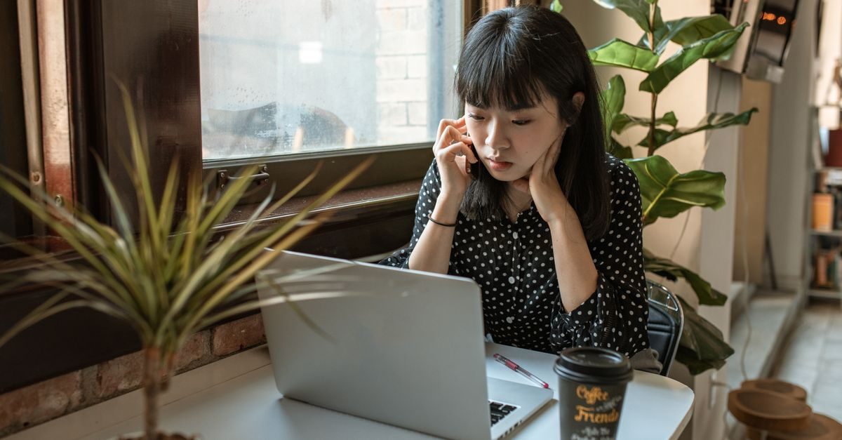 Jeune femme concentrée travaillant sur son ordinateur portable dans un café avec une plante verte à côté d'elle