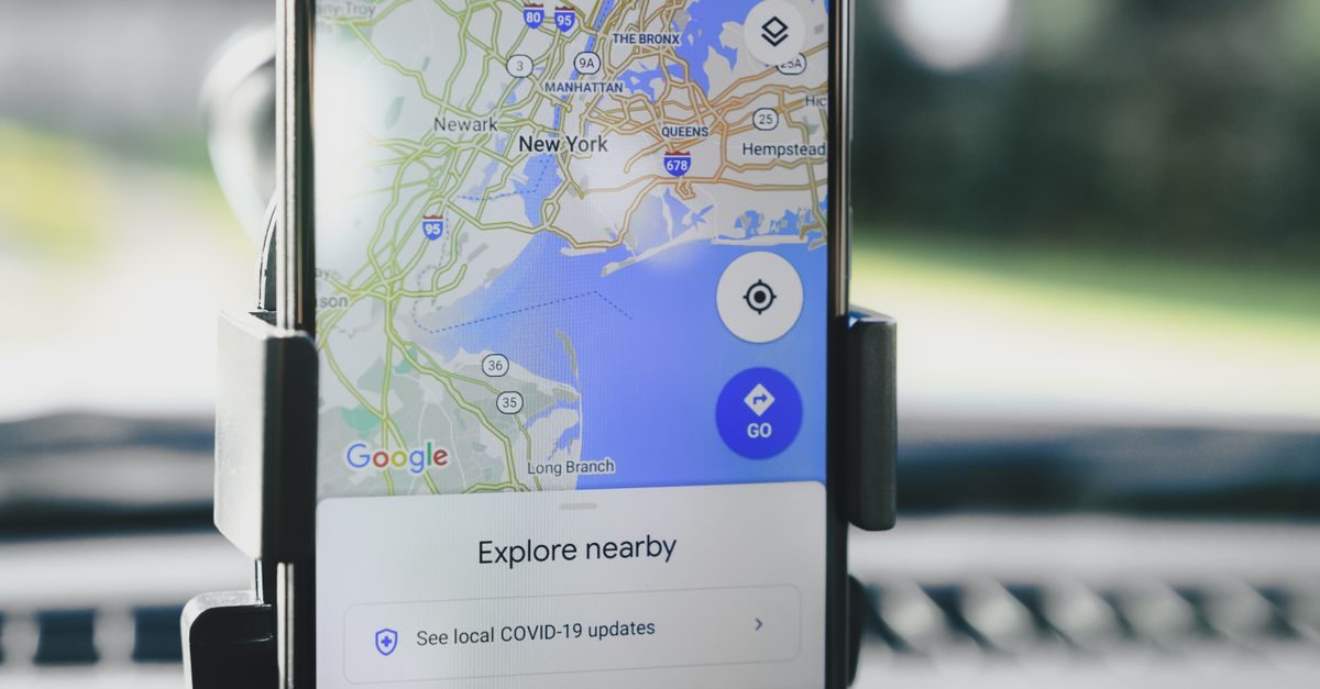 Smartphone mounted in a car displaying a Google Maps interface of the New York area with an explore nearby prompt