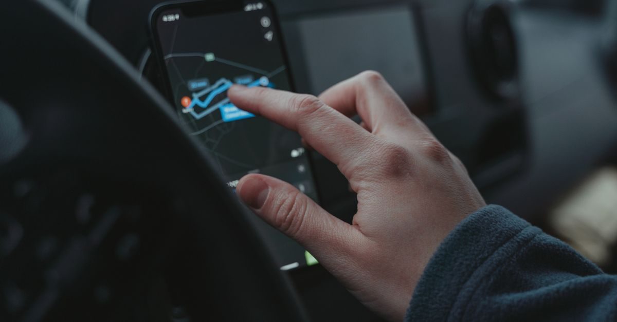Mano che utilizza un'app di navigazione su uno smartphone all'interno di un'auto in un contesto di guida urbana