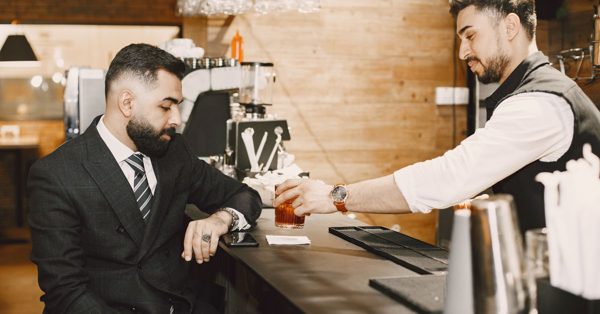 Un serveur sert un verre à un homme en costume assis au comptoir d'un bar dans une ambiance feutrée