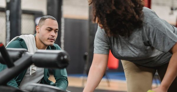 Ein Trainer berät eine Sportlerin im Fitnessstudio bei der Nutzung eines Trainingsgeräts in konzentrierter Atmosphäre