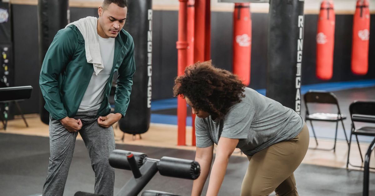 Ein Trainer beobachtet konzentriert eine Frau beim Training an einem Fitnessgerät in einem Boxstudio