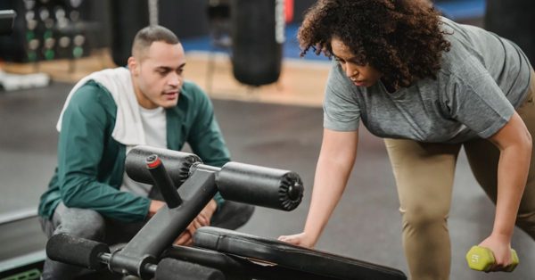 Un entrenador observa con atención a una mujer que realiza ejercicios con mancuernas en un gimnasio