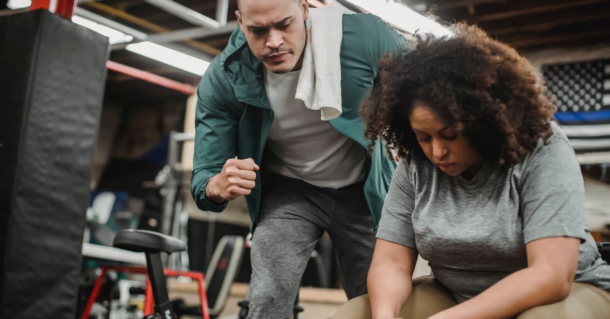 Entrenador personal motiva a una mujer concentrada en su ejercicio dentro de un gimnasio con ambiente enfocado y serio