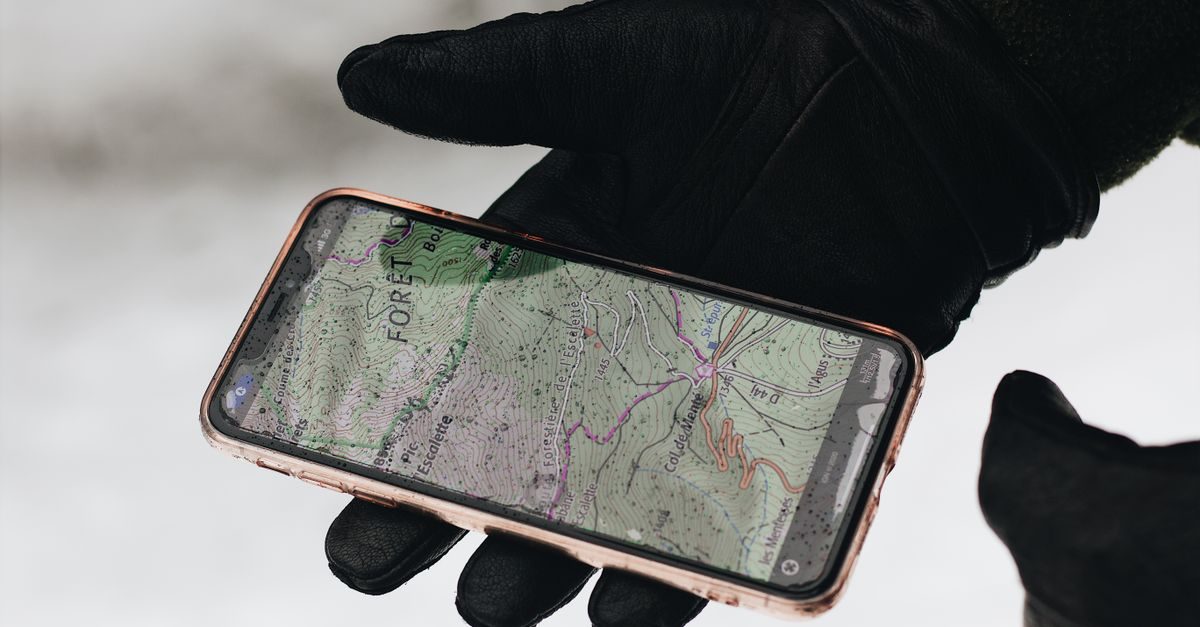 Main gantée tenant un smartphone affichant une carte topographique en extérieur par temps froid