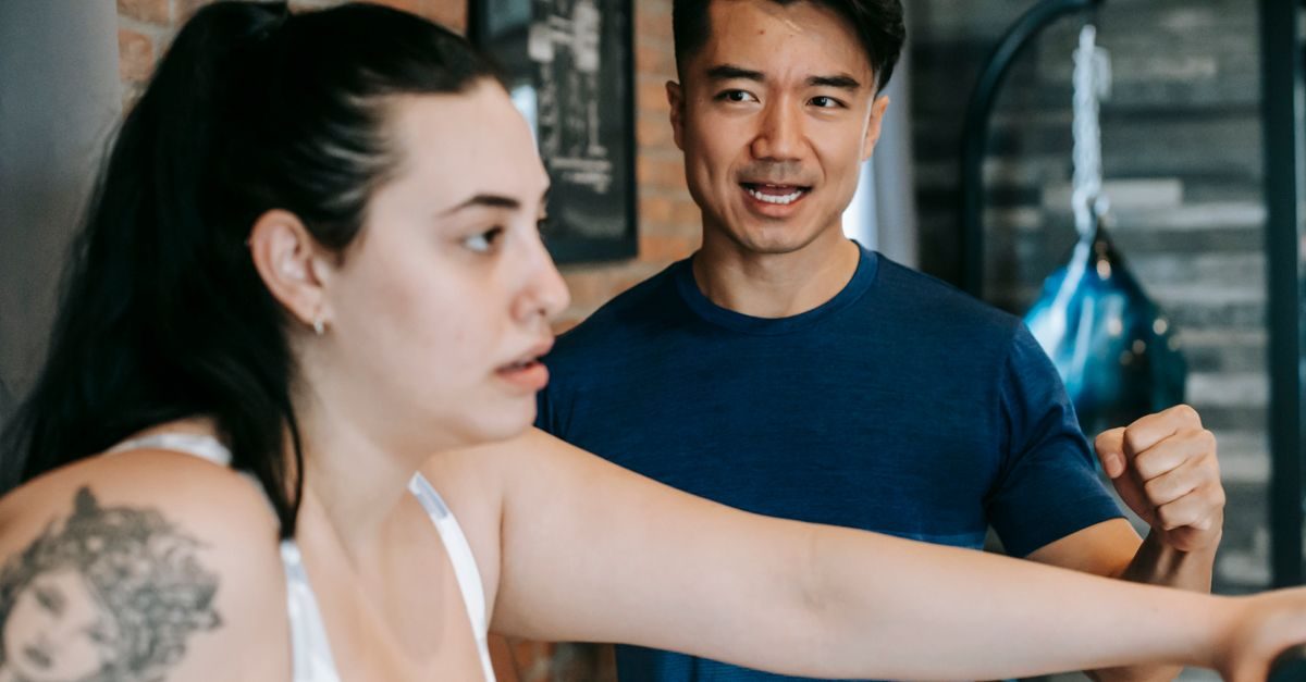A male personal trainer encourages a woman working out on a machine in a gym setting