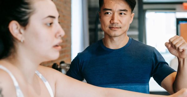 Ein Trainer beobachtet konzentriert eine Frau beim Training an einem Fitnessgerät in einem Studio