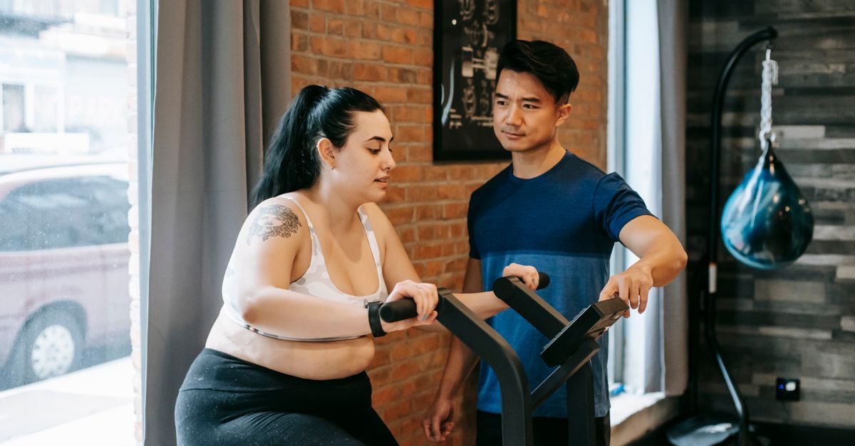 Ein Personal Trainer gibt einer Frau beim Training an einem Fitnessgerät in einem Studio mit Backsteinwand Anleitung