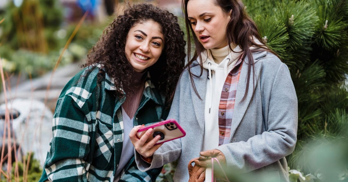 Deux jeunes femmes souriantes regardent ensemble l'écran d'un smartphone dans un environnement extérieur verdoyant