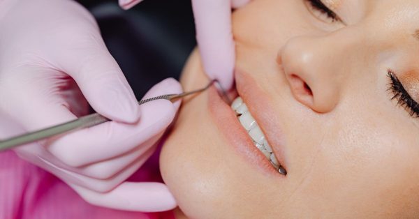 Stomatolog w różowych rękawiczkach wykonuje badanie uzębienia pacjentki przy użyciu narzędzia dentystycznego