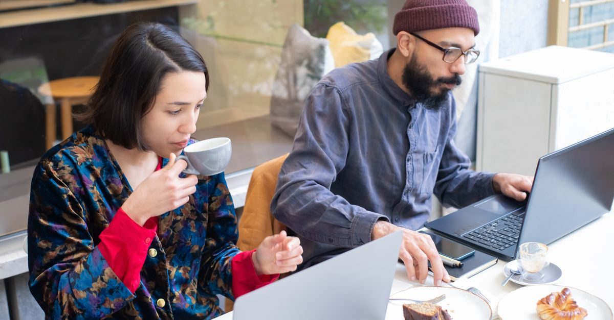 Man en vrouw werken geconcentreerd op laptops in een café terwijl ze koffie drinken en eten