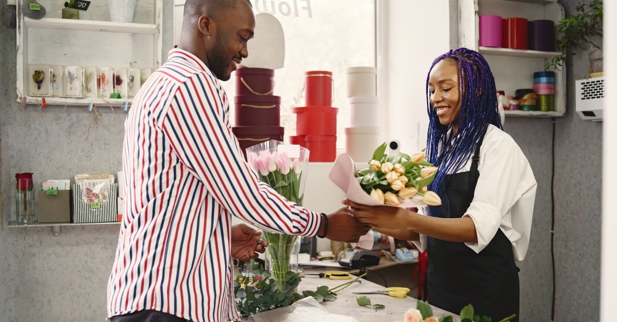 Une fleuriste souriante remet un bouquet de tulipes à un client dans sa boutique décorée de boîtes colorées