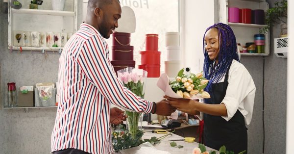 Une fleuriste souriante remet un bouquet de tulipes à un client dans sa boutique décorée de boîtes colorées