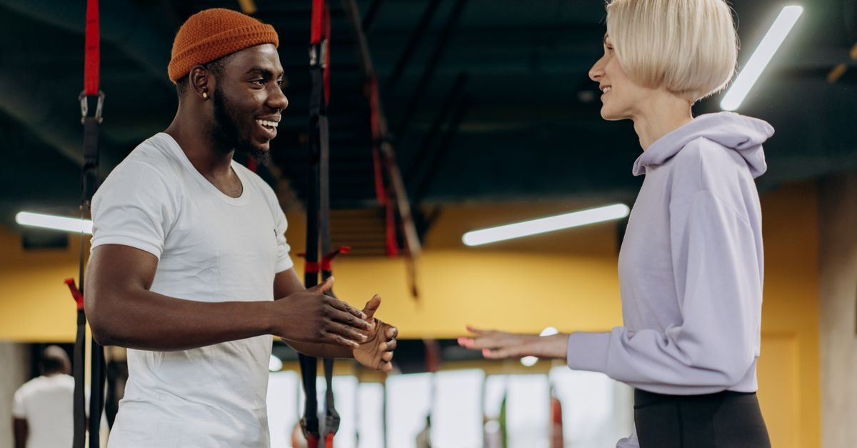 Un uomo e una donna sorridenti interagiscono in una palestra moderna tra cinghie per allenamento in sospensione