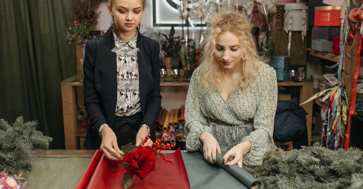 Två unga kvinnor arbetar fokuserat med att slå in blommor på en disk i en blomsterbutik