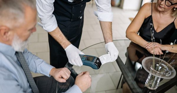 Ober met witte handschoenen overhandigt een betaalbon aan een echtpaar aan een glazen tafel in een restaurant