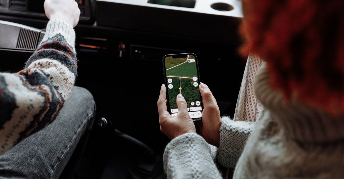 Dos personas con suéteres de lana viajan en coche mientras una sostiene un teléfono con un mapa de navegación abierto