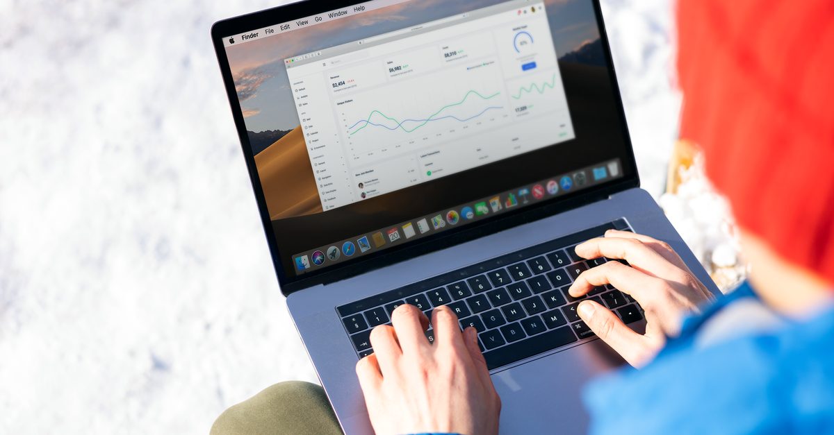 Iemand typt op een laptop met een dashboard vol grafieken en data in een buitenomgeving met sneeuw op de achtergrond