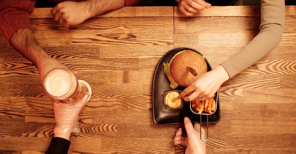 Persone sedute a un tavolo di legno che mangiano un hamburger con patatine e bevono birra in un'atmosfera conviviale