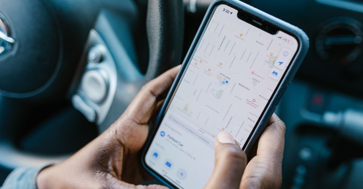 Mains tenant un smartphone affichant une application de cartographie depuis le siège conducteur d'une voiture
