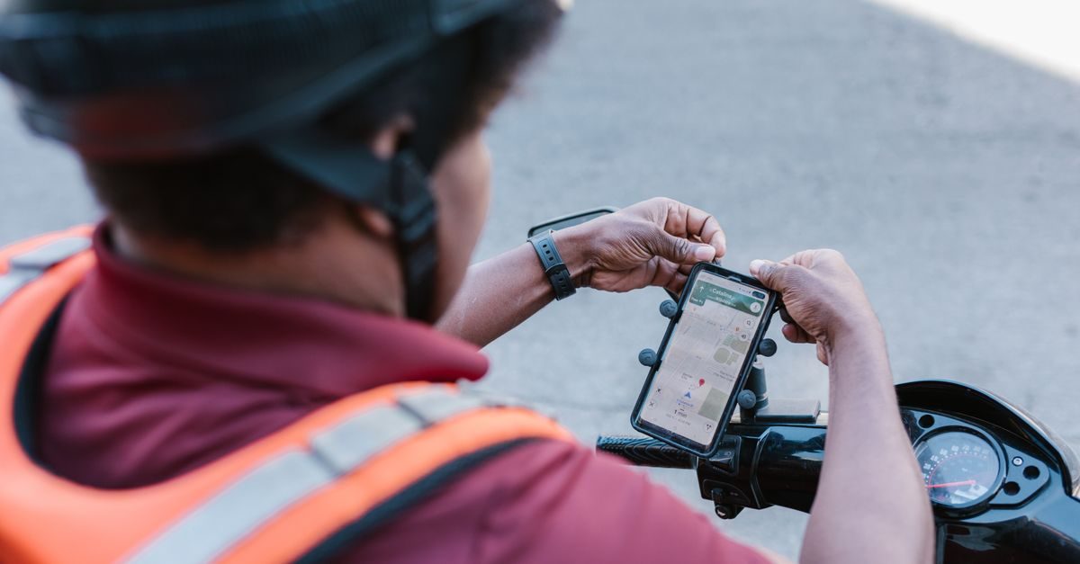 Un livreur à vélo portant un casque ajuste son smartphone fixé sur le guidon pour consulter un itinéraire sur une carte