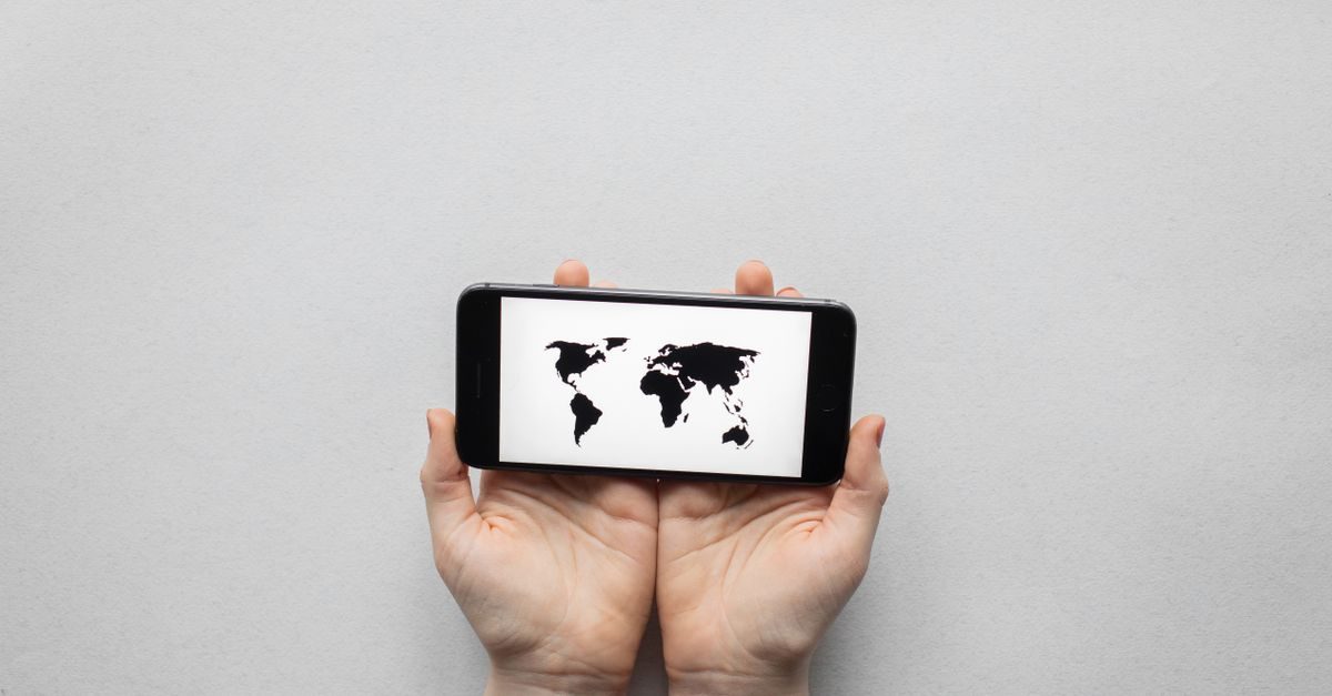 Hands holding a smartphone displaying a black and white world map against a plain gray background