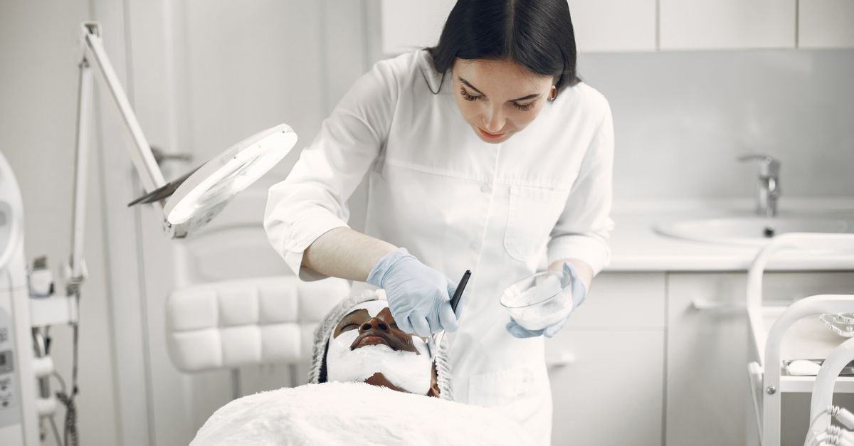 Estetista in camice bianco applica una maschera viso a una cliente in un centro estetico luminoso e professionale