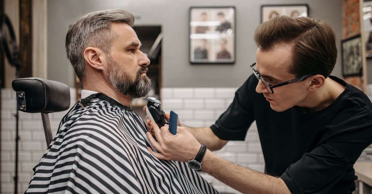 Kapper in zwarte kleding trimt de baard van een klant in een professionele salon met een gefocuste blik