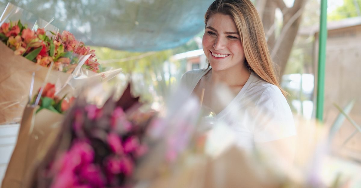 Una giovane fioraia sorridente lavora nel suo negozio circondata da colorati bouquet di fiori freschi incartati