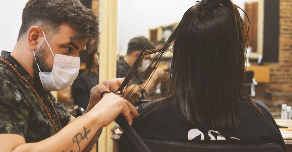 Ein Friseur mit Mundschutz schneidet konzentriert die Haare einer Kundin in einem professionellen Salon