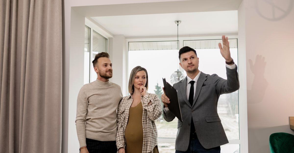 Agente immobiliare in giacca mostra una casa a una giovane coppia in attesa in un luminoso ambiente moderno e accogliente