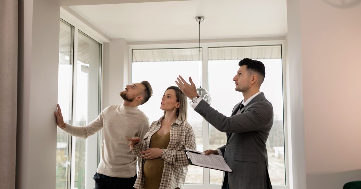 Makelaar in pak geeft uitleg aan een jong stel tijdens een bezichtiging van een lichte woning