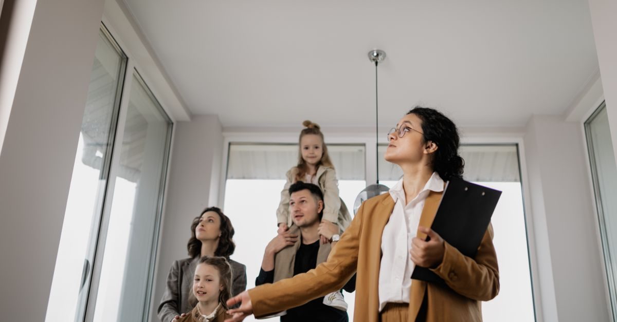 Makelaar in beige pak geeft rondleiding aan een jong gezin in een licht appartement met grote ramen
