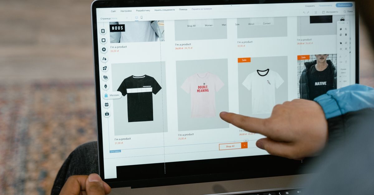 A person points at a t-shirt displayed on a laptop screen while editing an online store website layout