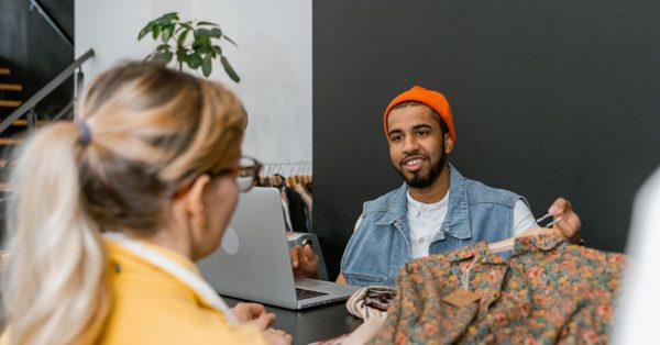 Un homme en bonnet orange et une femme discutent devant un ordinateur portable dans une boutique de vêtements