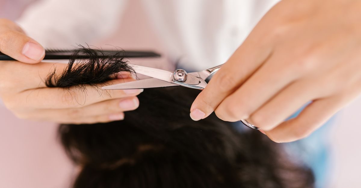 Manos de peluquero cortando un mechón de cabello oscuro con tijeras y un peine en un salón de belleza