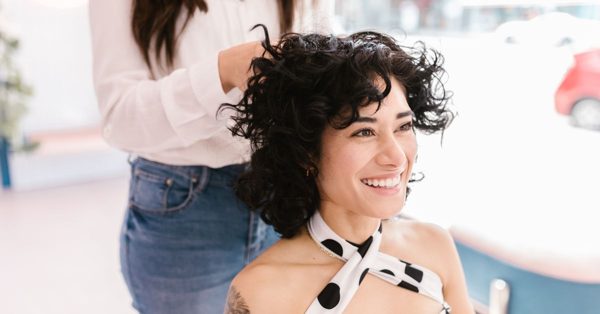 Une coiffeuse ajuste les cheveux bouclés d'une cliente souriante dans un salon lumineux