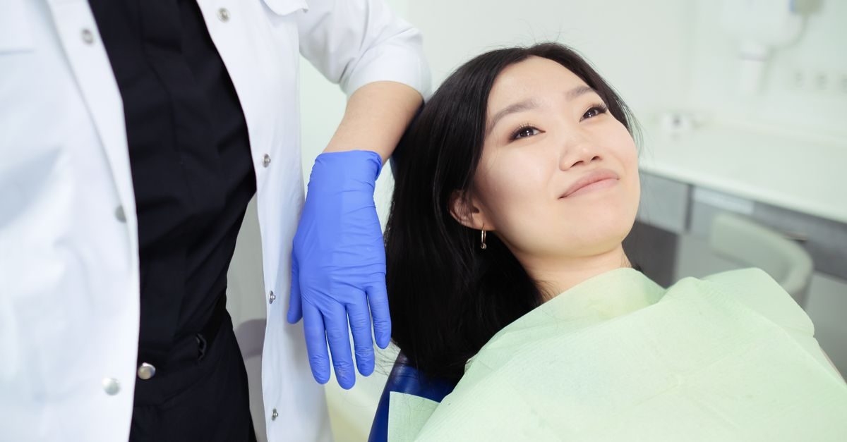 Dentista con bata blanca y guantes azules junto a una paciente sonriente en un consultorio odontológico moderno