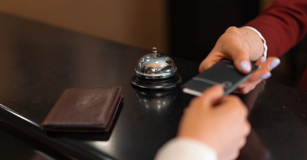 Mani consegnano una carta magnetica alla reception di un hotel accanto a un campanello e un portafoglio su un bancone