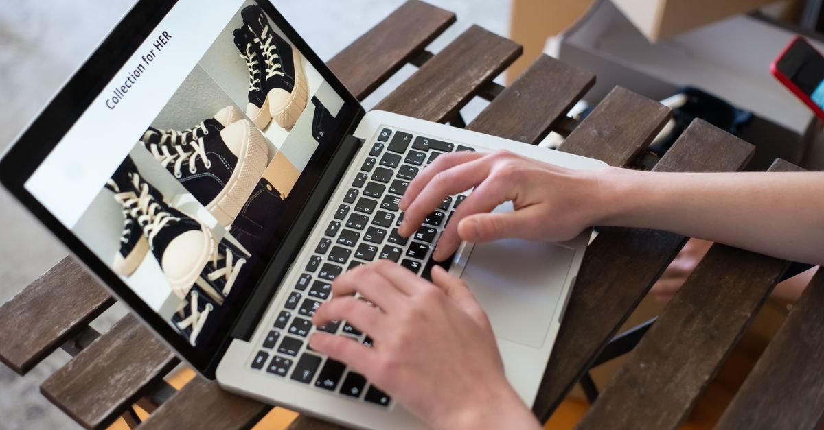 Manos escribiendo en un portátil sobre una mesa de madera mientras navegan en una tienda online de calzado