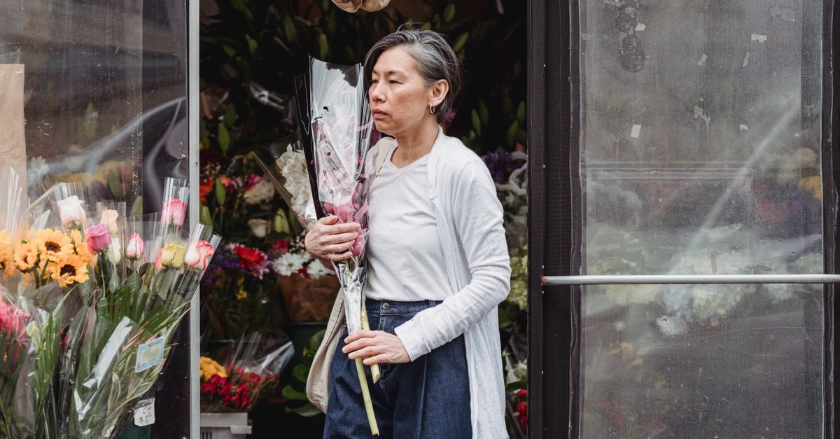 Vrouw met grijs haar houdt een boeket bloemen vast bij de ingang van een bloemenwinkel