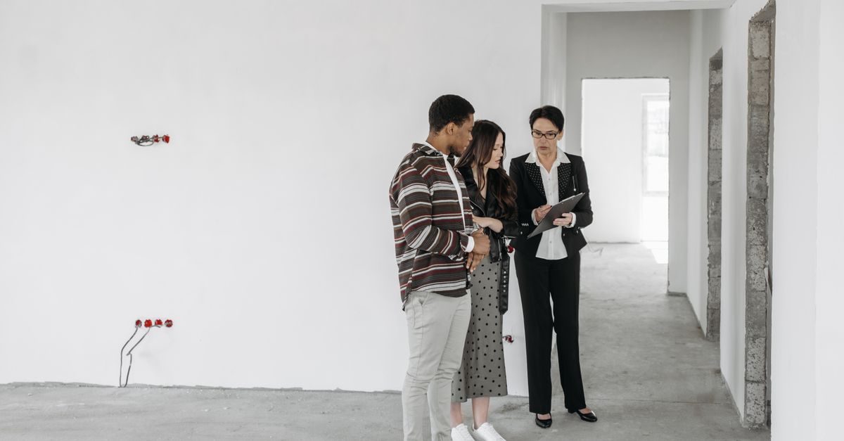 Une agente immobilière présente un document à un jeune couple dans un appartement en cours de rénovation