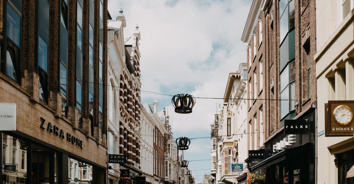 Winkelstraat met historische gevels, winkels zoals Zara Home en Falke, en kroonvormige decoraties boven de weg