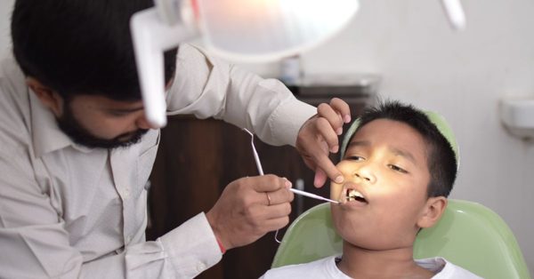 Dentista visita un bambino seduto sulla poltrona dello studio odontoiatrico utilizzando uno specchietto professionale